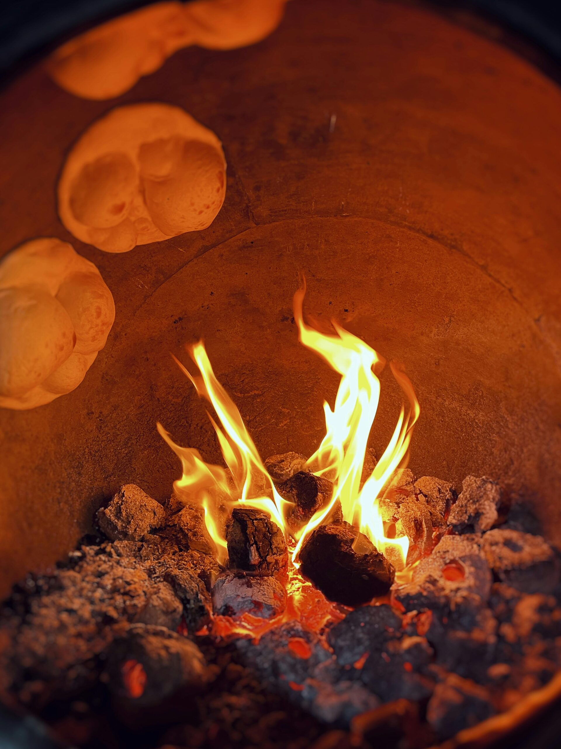 Flames inside a clay tandoor oven baking traditional bread. Warm and rustic culinary setting.